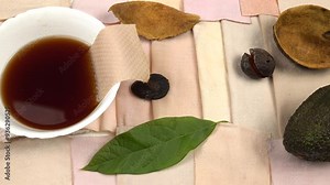 Bowl of avocado peel and pit decoction, avocado fruit, dried peel, avocado leaf are on the samples of cotton fabric in gradient dusty rose color Stock Video