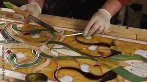 Skilled workman is processing copper tape of stained-glass panel. He is using tin solder and soldering iron, assembling and fixing beautiful hand made stained-glass