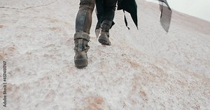 Close-up following shot of female legs stepping. Wide angle post apocalyptic female in futuristic grunge black clothes feet climbing hill in dead desert. Cyberpunk future warrior survivor after war