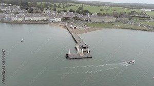 Beaumaris Seaside town With Pier And Coast, Wales. Aerial view ascending dolly right across Menai Strait tourism coastline. Boat moving through lower scene.