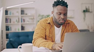 Concentrated black man typing on laptop and taking notes in notepad, freelance Stock Video