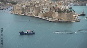 A ship towing fish farming equipment across the Grand Harbour, Valletta