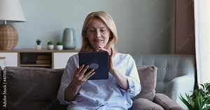 Concentrated older lady rest on comfy sofa on weekend surf web pages on modern digital pad check email choose consumer goods online at ecommerce store. Happy smiling aged female use touchpad at home