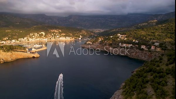 4K Aerial Drone video of popular summer destination, sunset over the cliffs with a lighthouse and a huge port of boats anchored at golden hour with seagulls flying. Port de Soller, Mallorca