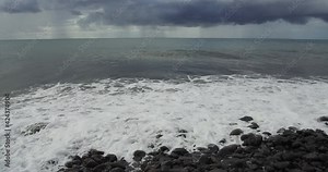 Waves hitting a pebble beach with heavy rain off-coast Reunion Island.