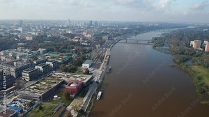 Forwards fly above Vistula river calmly flowing through town. Modern building of Copernicus Science Centre with planetarium on riverbank. Aerial panoramic view. Warsaw, Poland