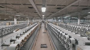 glass fiber production at the factory, macro fiberglass stretches through holes at plant. closeup large loom weaves white synthetic fiber
