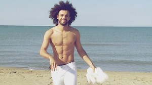 Happy athletic male model taking off shirt slow motion while walking towards camera in summer in front of the ocean