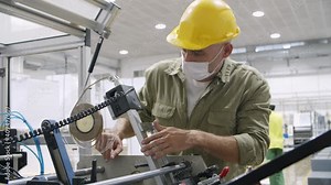 Skilled engineer in facial mask repairing factory equipment. Confident focused technician in protective uniform checking machine and looking inside it. Visual inspection and manufacture concept