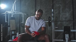 Fitness workout in gym. African American man fighter preparing for fight wrapping hands with red boxing wraps sports protective bandages in gym. Strong man ready for fight boxing sparring training