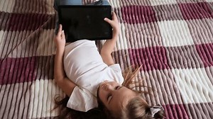 Child girl playing with digital wireless tablet computer on bed at home.