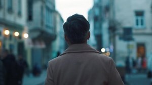 Back view of unrecognizable man walks along the city center street looks around city lights on background business downtown evening happy close up slow motion