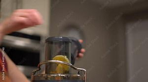 Woman putting variety of different fruits into top of electric juicer to make healthy fresh fruit juice - female caucasian hand putting sliced fruits in juicer electric kitchen appliance close-up