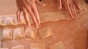 4k slow motion top down view of the cook wife's hands pressing with fingers and cutting the strip of filled pasta with the wheel to shape ravioli or green tortelli. Traditional homemade food recipe