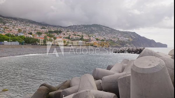 Wave breakers near Atlantic ocean shore with city in background, Madeira