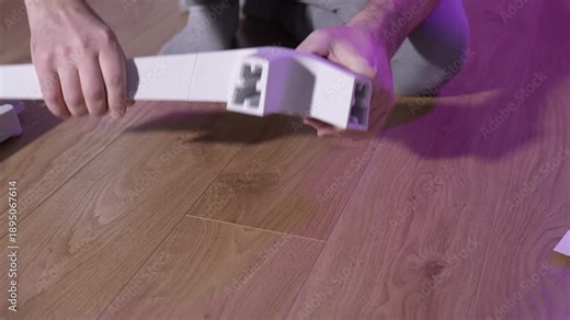 Man assembling office chair base by inserting legs into plastic hub on wooden floor, close-up view, DIY furniture assembly at home.