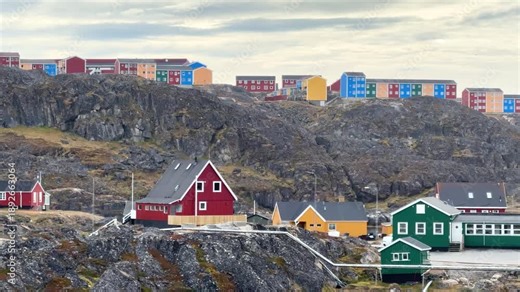 Colorful houses in Greenland near the coastline. The area has colorful houses and rocky terrain. The sky is cloudy, giving a unique view of the landscape.