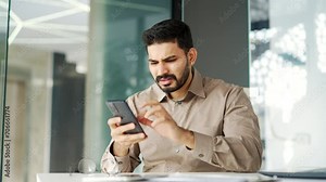 Frustrated businessman having problems with software or service on smartphone mobile phone sitting at workplace in business office. Worried disappointed worker complains about bad internet connection