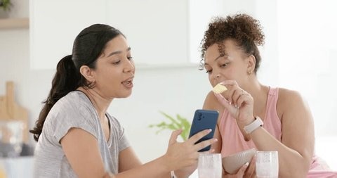 clip-4047241323-showing-two-women-scrolling-blue-phone-kitchen
