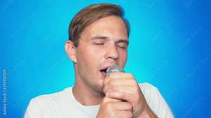 a crazy funny young man sings songs into a microphone. color background, close-up. 4k, slow motion