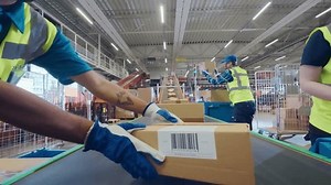 Workers in High-Visibility Vests Place a Package with a POV Camera Along a System of Conveyor Belts in a Distribution Hub. Camera Moving in Large-Scale Retail E-Commerce Logistics Service