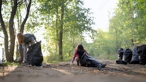 Female volunteers finish cleaning in nature. The girls put a large garbage dump in plastic bags. Nature has become cleaner, pollution has been eliminated.