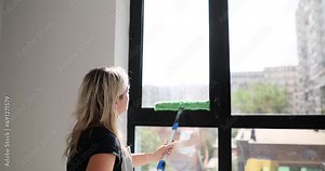 Woman washes windows with long mop and brush