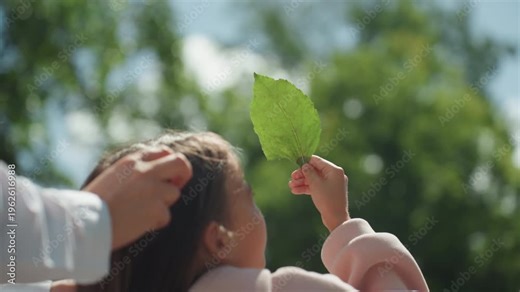 Kid explores plant. Young girl discovering leaf features. Child investigates leaf details with gentle guidance. Young girl examines detailed aspects of leaf while being supported by her mother