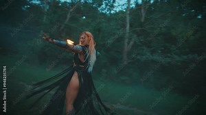 Gothic woman witch sorceress shaman holds burning stick torch flame light spinning dancing ritual dance whispers creates magic spell in dark night forest. Black dress macrame rags flies slow motion 4k