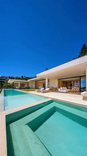 Designed as a quiet retreat on an elevated site, Halcyon Residence focuses on simplicity, light, and connection to nature. A raised concrete platform captures sweeping views, while sliding glass doors open living spaces directly to gardens, terraces, and a pool—blurring the threshold between indoors and out. Below, a private wellness level with a gym, media room, and guest suite opens to its own side courtyard, creating a secluded escape tucked into the hillside. A palette of travertine, oak, an