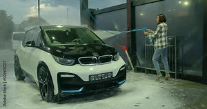 Woman with a hose with water in her hands washes the car