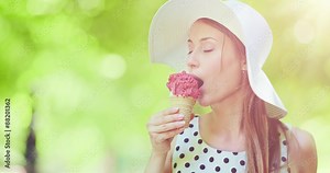 Beautiful woman eating ice cream in the park. Slow motion, portrait. Stylish young attractive woman in white hat enjoying tasty ice cream and nature in the green sunny summer outdoors. 4K, DCi.