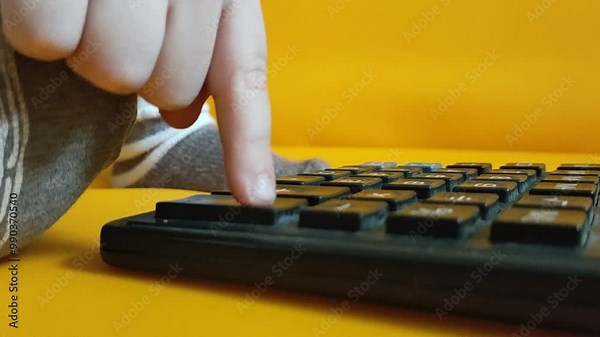 Child hands with calculator counting during school homework. Kid fingers press buttons and calculate studying math at home. A small child counts on a calculator on a yellow background