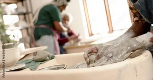 Hands of african american male potter using potter's wheel in pottery studio, slow motion