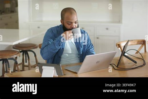Man sipping mug while scanning laptop, spotting surprise, leaning and typing on tablet for business. Computer, cup, remote, minimal, tech, kitchen, dining Stock Video Footage - Alamy