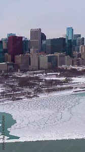 Urban Skyline of Chicago Loop and Frozen Lake Michigan with Ice Lumps on Winter Frosty Day. Aerial View. United States of America. Drone Flies Sideways, Tilt Up. Vertical Video