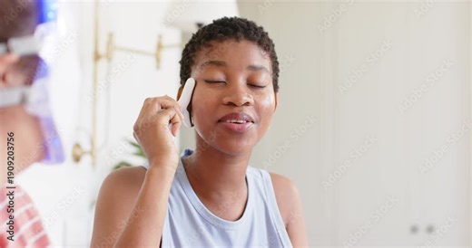 Woman receiving treatment at home vanity, holding device while tech guiding as green LED lighting