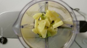 Pinapple chunks are thrown into blender to make smoothie. vegan drink for healthy living and keeping fit is going to be prepared in kitchen at home.