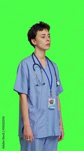 Side view Young nurse with medical expertise poses with confidence, wears blue scrubs uniform and smiling against greenscreen backdrop. Health assistant gives support to doctors as profession. Camera