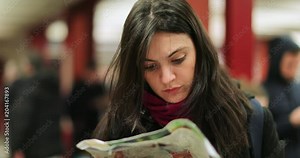 Woman checking paper map for directions. Authentic candid real life person looking at map to know where to go while on underground subway platform in 4K