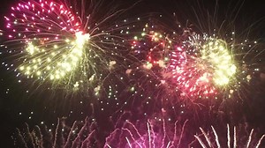 Colorful fireworks exploding in night sky. Crowd enjoying the beautiful fireworks display in sky during New Year celebration. People watching fireworks show. Handheld