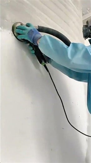 smoothing a white plaster layer on a grey concrete wall surface using a circular electric sander