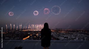 A stunning city skyline celebration with fireworks illuminating the night sky and a silhouette watching from a rooftop