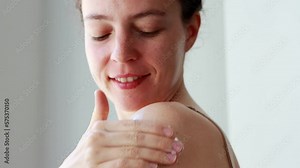 Young brunette woman applying suntan solar cream to her shoulder,do daily routine nourishing smoothing body lotion after shower.Beauty and healthy skin care treatment concept.Sunscreen spf protection