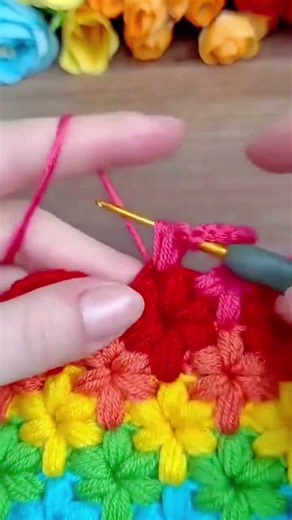 making colorful flower patterns with pink yellow blue and green wool by using small metal crochet
