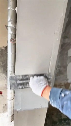 applying grey cement plaster to vertical wall surface using a metal trowel tool carefully