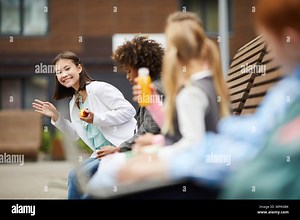 Asian girl smiling and waving her hand she greeting her friends while they sitting together on the bench outdoors Stock Photo - Alamy