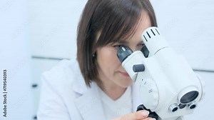 A gynecologist woman looks into a microscope taking a close-up.