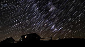 Time lapse of comet-shaped star trails over Wooden house in the night sky. Stars move around a polar star. 4K