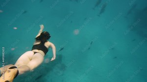 Beautiful young woman swimming underwater with dolphins in pristine blue ocean water, amazing snorkeling adventure. Armature freediver girl diving in red sea with bottlenose dolphins. Travel concept